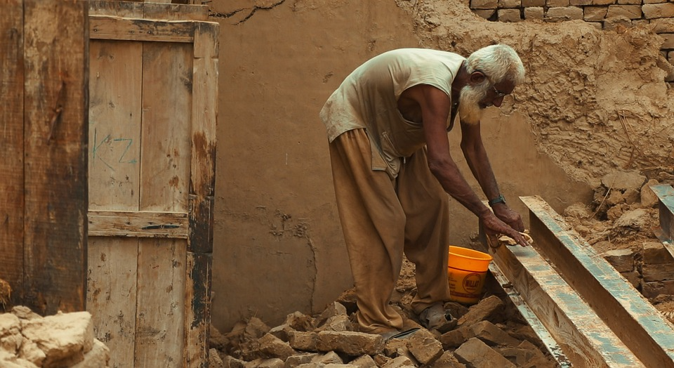 An old age person removing reusable things from his destroyed house after flood